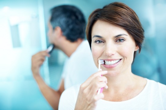Smiling mature woman brushing her teeth while her partner shaves - portrait